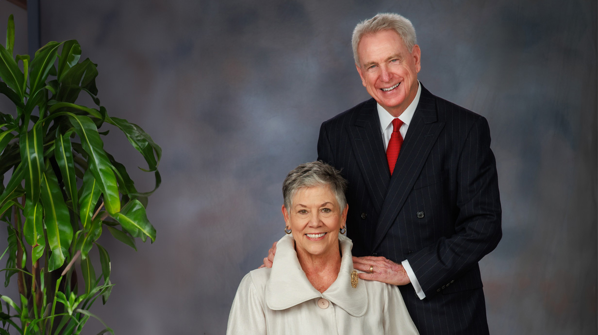A man and woman pose for a formal portrait in front of a gray backdrop.