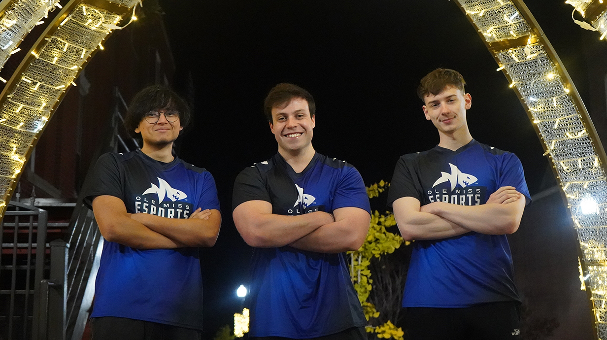 Three young men wearing matching blue jerseys with a shark logo stand with crossed arms in front of lighted arches.