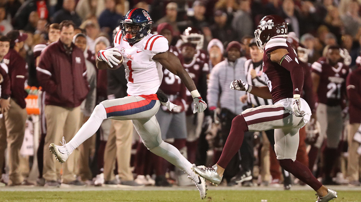 A football player carrying the ball runs form another player during a game in a stadium.