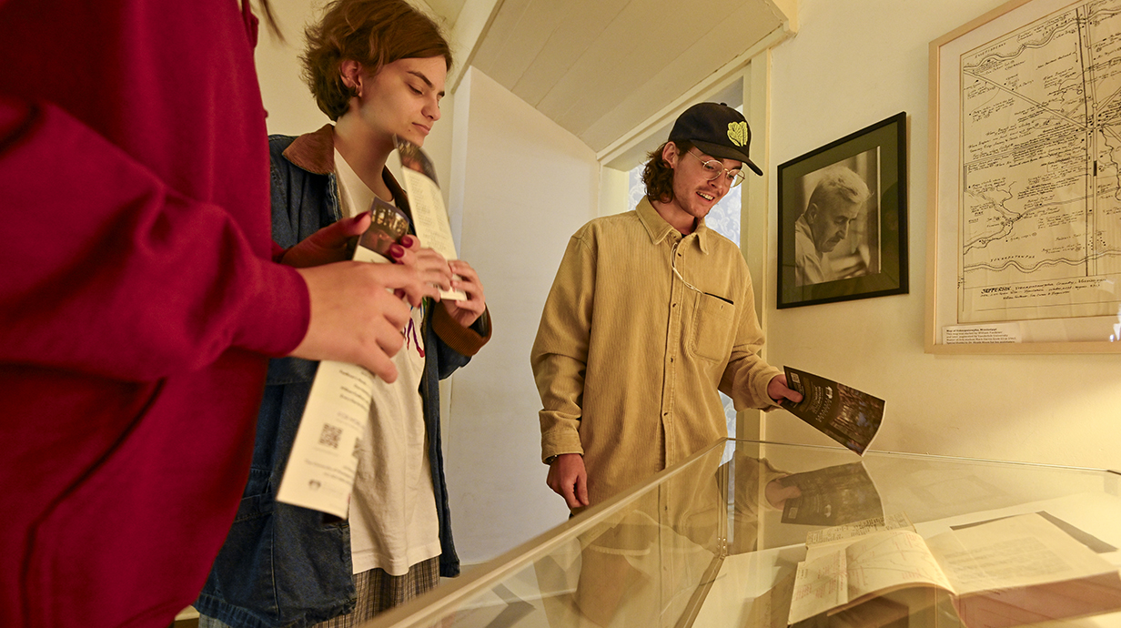 Three young people examine a large book in a glass display case.