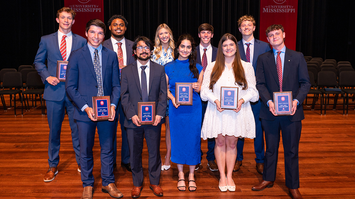 Ten young men and women, all dressed in formal attire, stand on a stage holding award plaques.