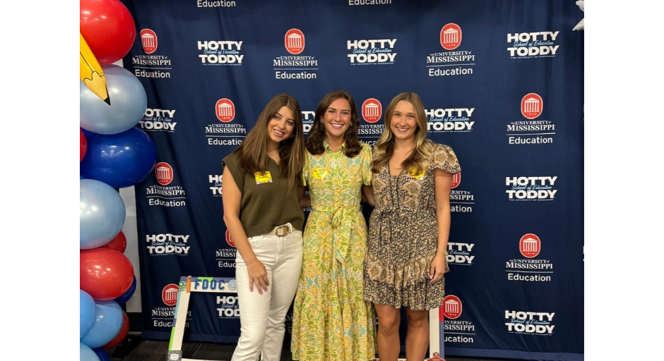 Sophie Humphreys (left), Keyes (center) and Hanna Honea (right) stand in front of a blue backdrop with various Ole Miss logos, celebrating the start of their senior year at the student teaching orientation in August 2024.