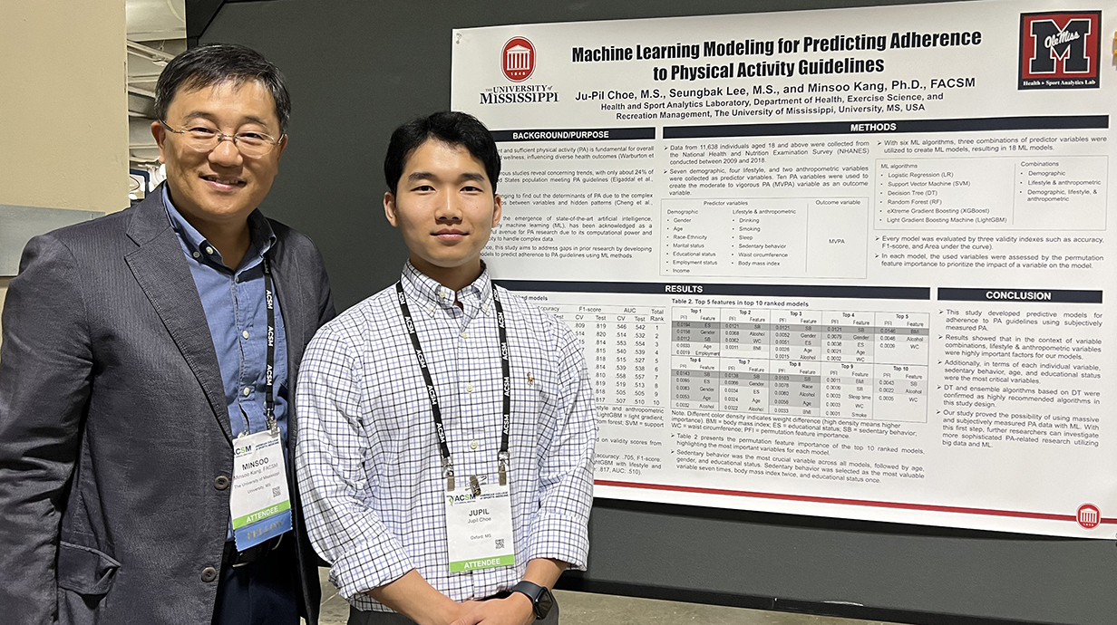 Two men wearing name tags stand in front of a research poster mounted on a gray backdrop.