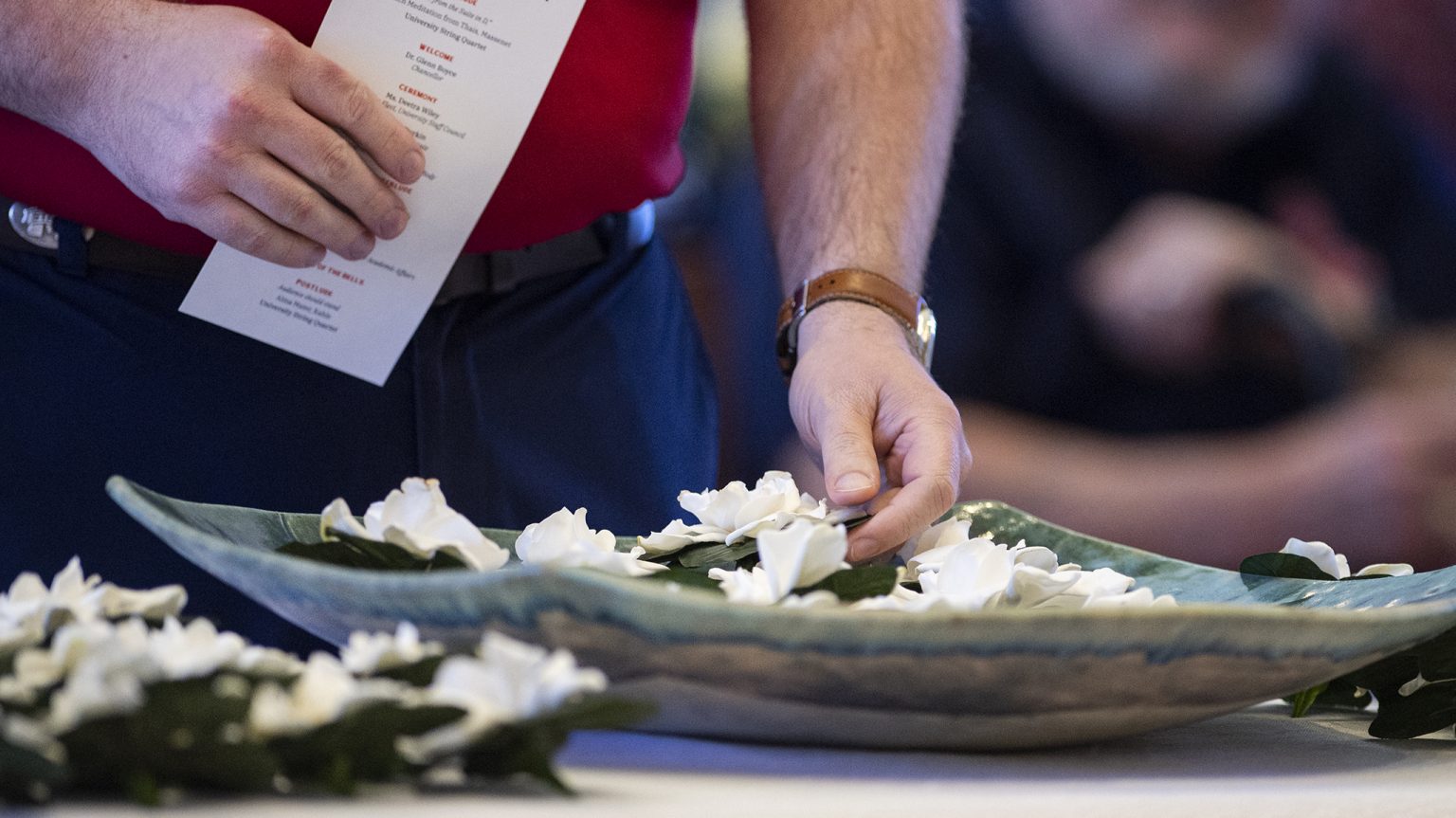 A hand placing a memorial flower in a bowl at a previous year's service.