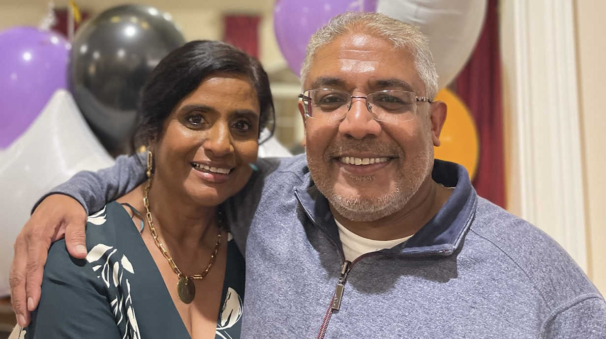 A man stands with his arm around a woman in front of a bunch of inflated party balloons.