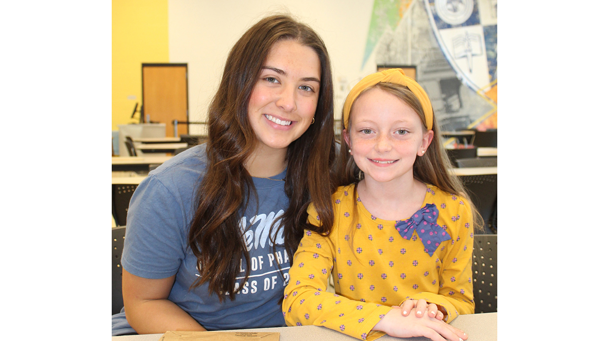 A young woman sits with a girl at a table.