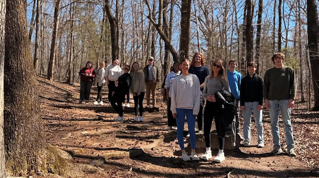A group of young people hike along a trail through the woods.