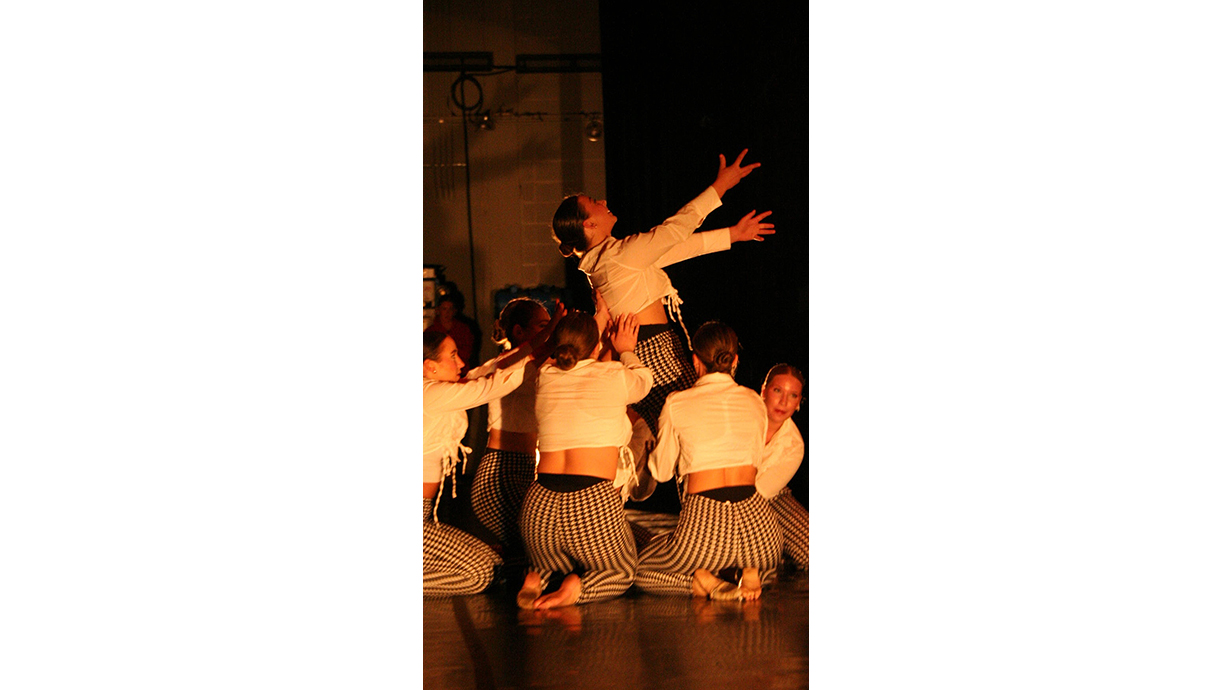 A group of dancers on a stage lift one dancer on their shoulders.