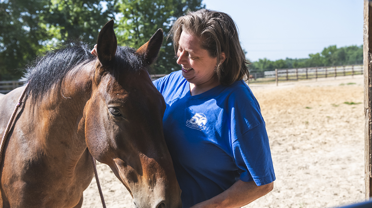A woman strokes a brown horse's neck in an outdoor pen.