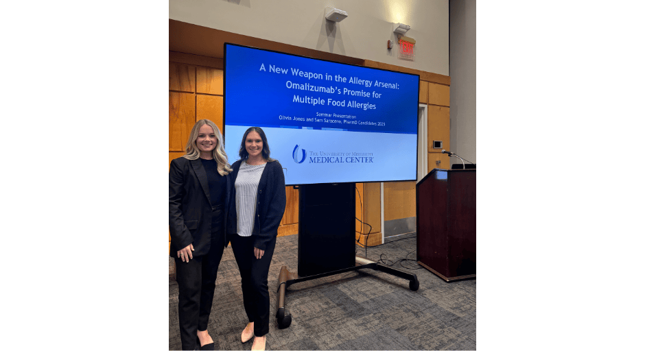 Olivia Jones and Samantha Saraceno stand in front of their presentation on managing multiple food allergies with a single new drug.