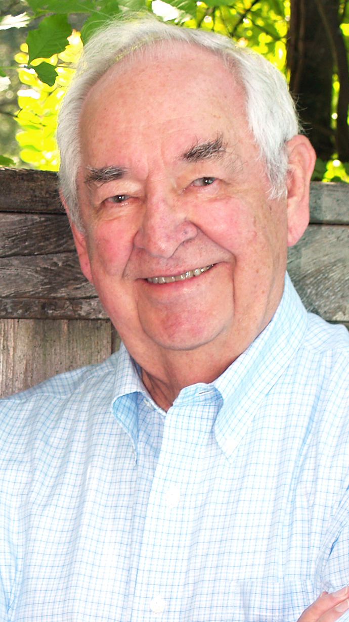Photo of a man standing outdoors next to a wooden fence.