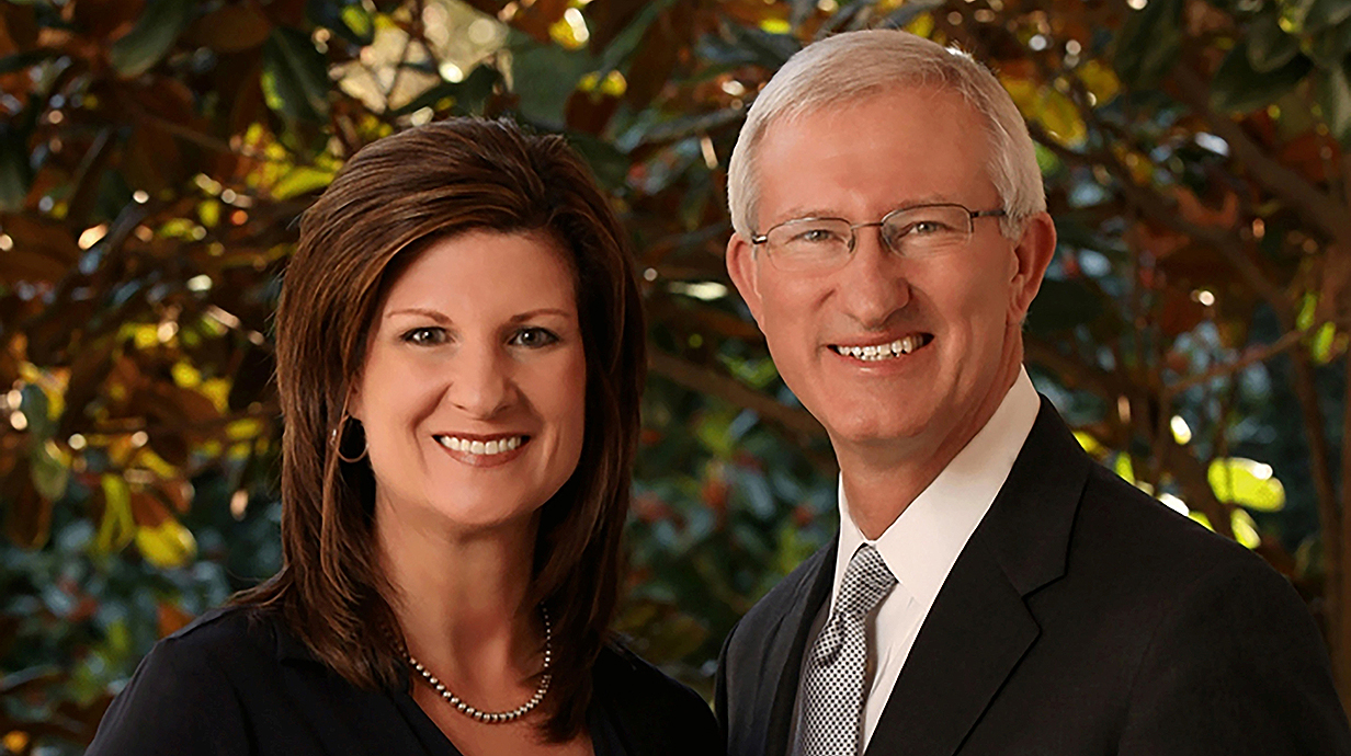 Outdoor portrait of a woman and a man standing together in front of a tree.