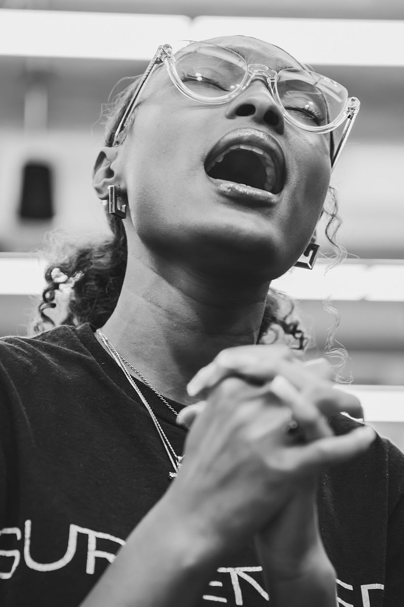 African American woman, Aaliyah Bishop, eyes closed and hands clasped lost in devotional music.