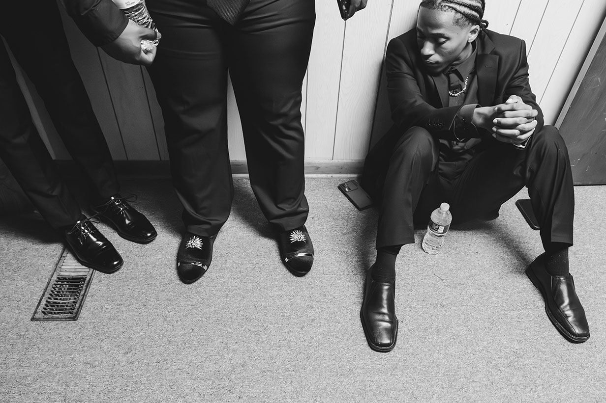 Group of male choir members dressed in black concert attire waiting backstage or in preparation area before their performance.