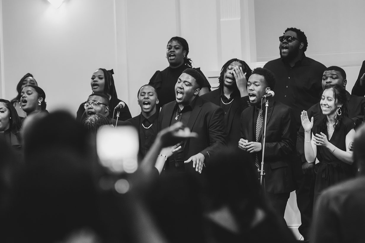 Gospel Choir members performing with raised hands and energetic expressions during their spring concert at Clear Creek Missionary Baptist Church.