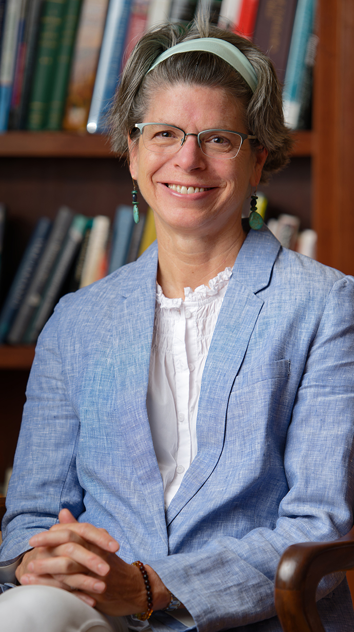 A woman sits in a chair in front of bookshelves.