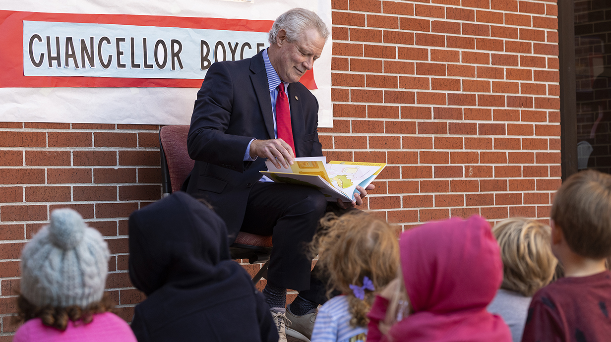 A man wearing a suit reads a book to a group of children.