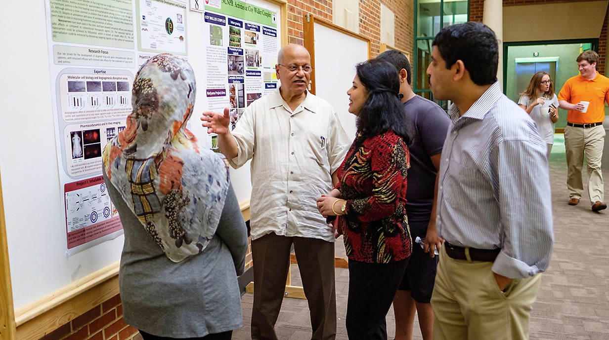 A man talks to a small group of young people looking at a research poster in a hallway.