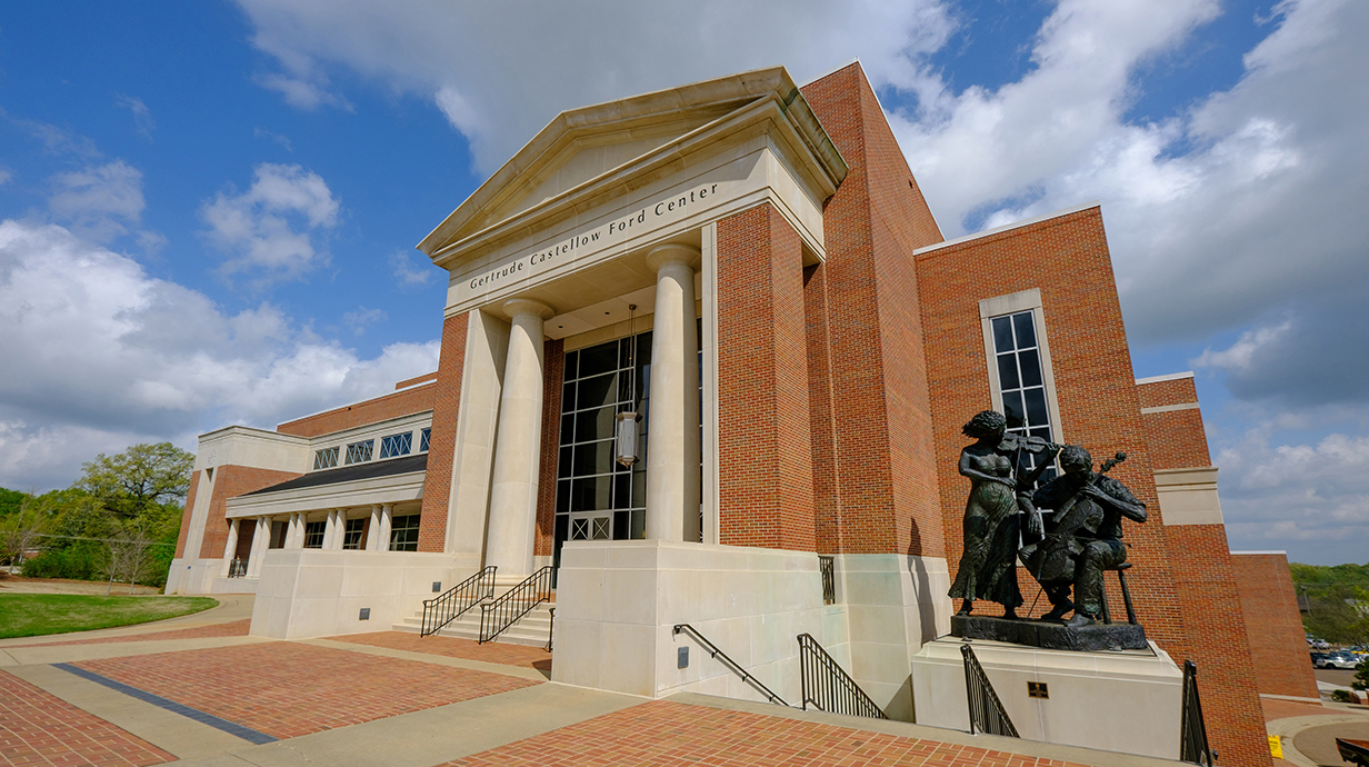 Photo of a large brick theater with a statue of musicians in front.