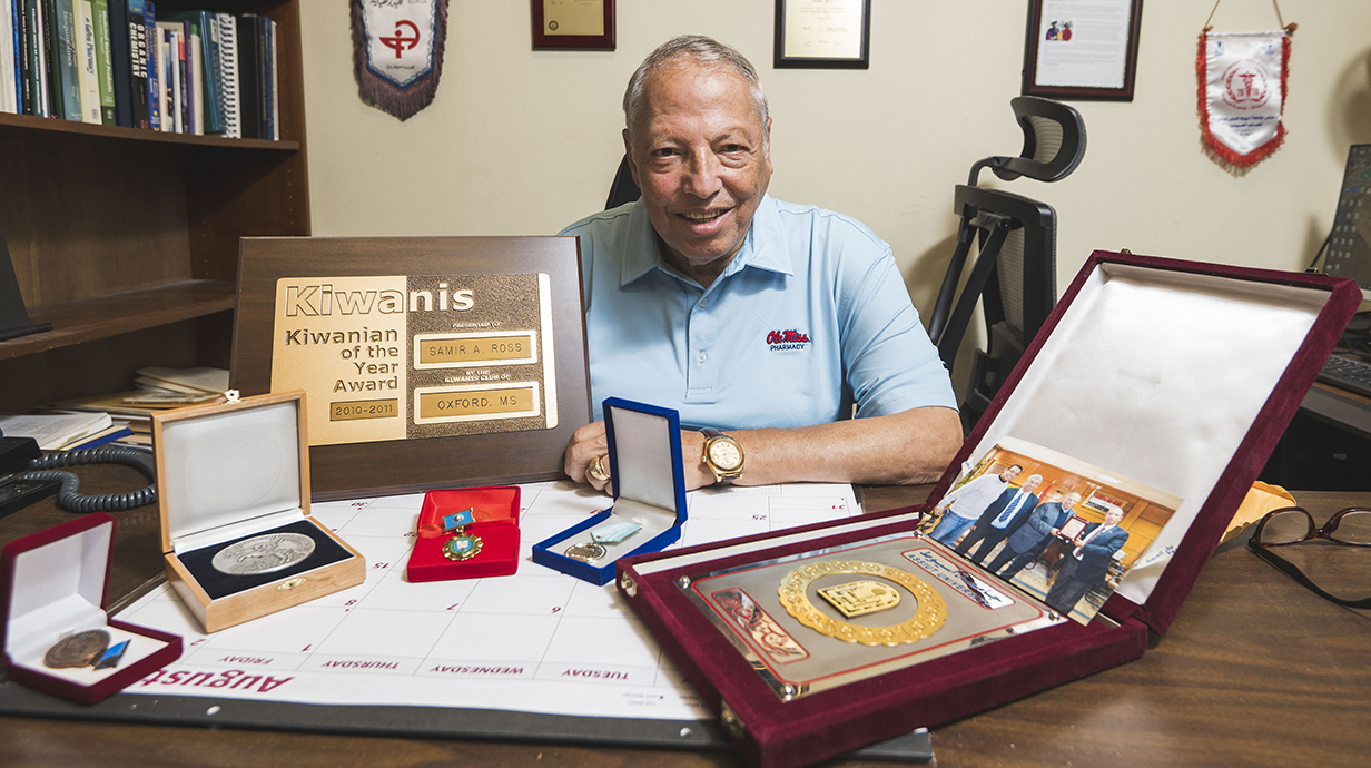 A man displays several awards and mementos on his desk.