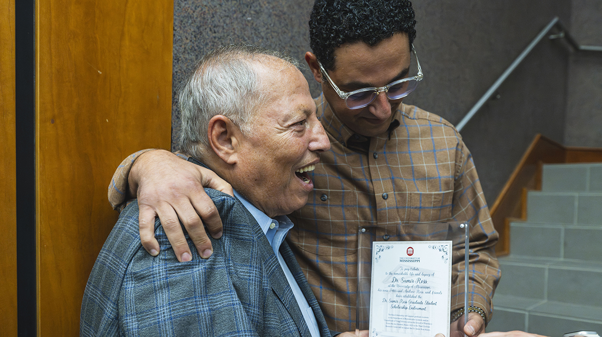 A young man presents a framed certificate to an older man.