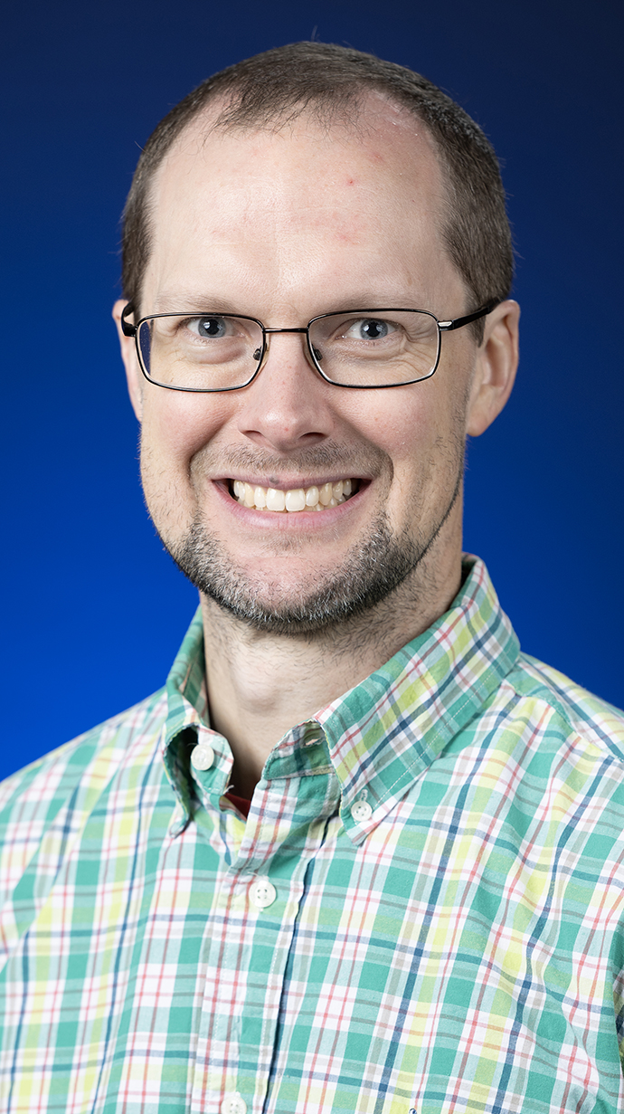 Headshot of a man wearing glasses and a green plaid shirt.