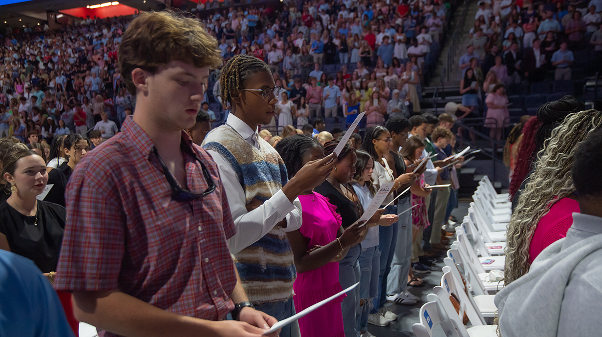 A large group of young people stand and read from flyers.