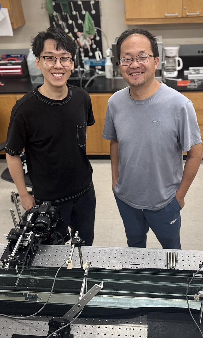 A young man looks through a camera mounted on a track in a lab while another man watches.