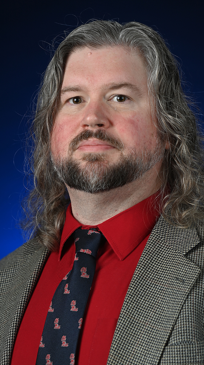 Headshot of a man wearing a coat, tie and a red shirt.