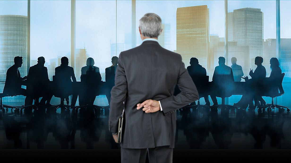 A man looks into a crowded boardroom with his fingers crossed behind his back.