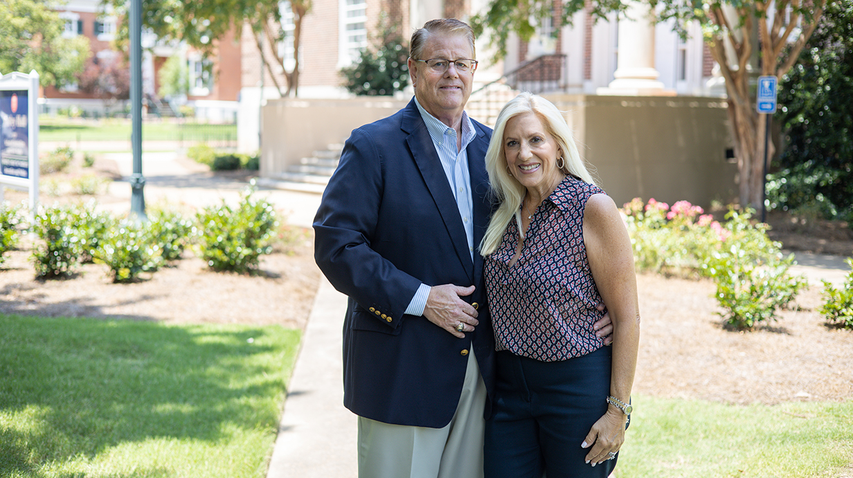 A man and woman stand outside a large brick building with white columns.