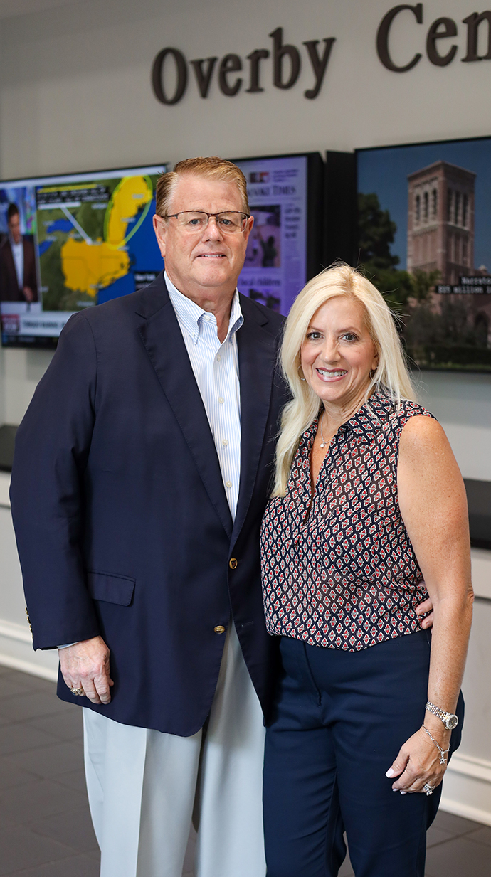 A man and woman stand in a hallway in front of a display reading 'Overby Center.'