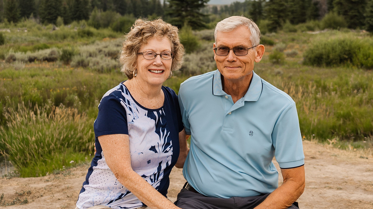 A man and a woman sit outside with a vacant field behind them.