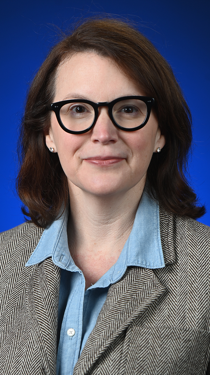 Headshot of a woman wearing glasses and a gray blazer over a blue blouse.