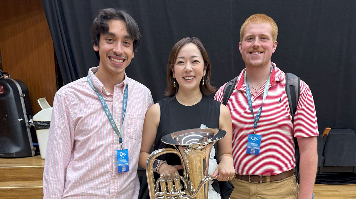 Two young men stand on a stage with a woman holding a euphonium.
