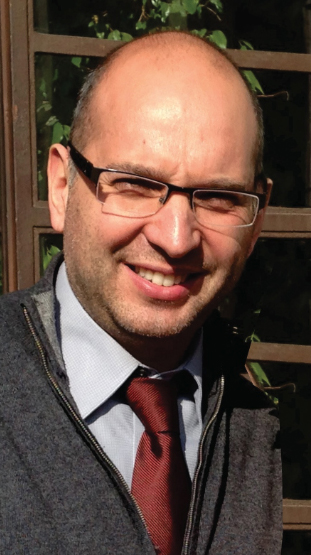 Headshot of a man wearing glasses and squinting in the sun.
