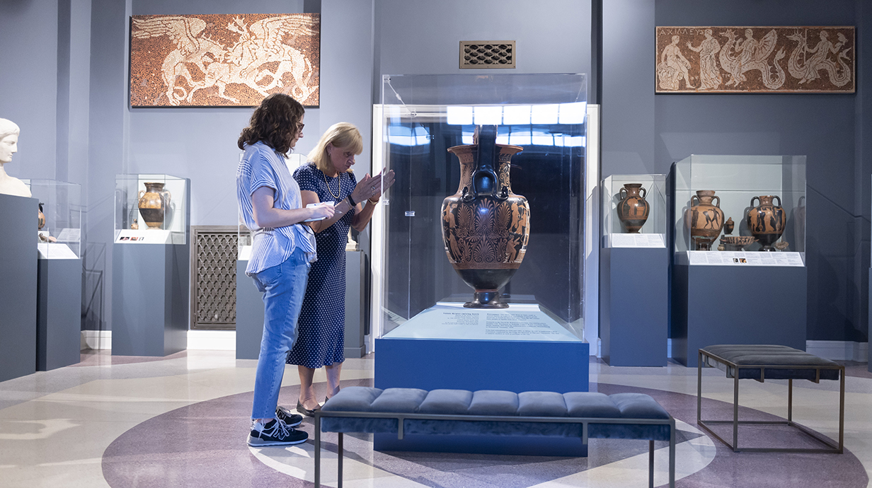 Two women look at elaborate pottery relics in a museum gallery.