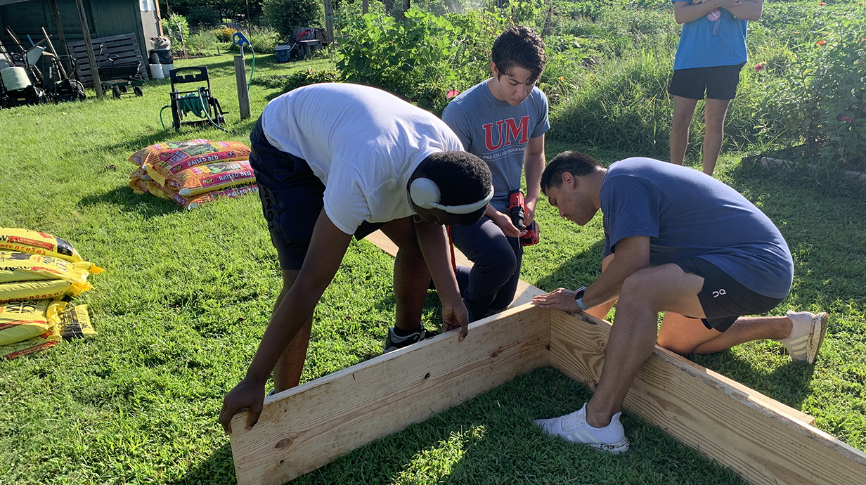 A man helps two young people construct the frame for a raised garden bed with lumber.
