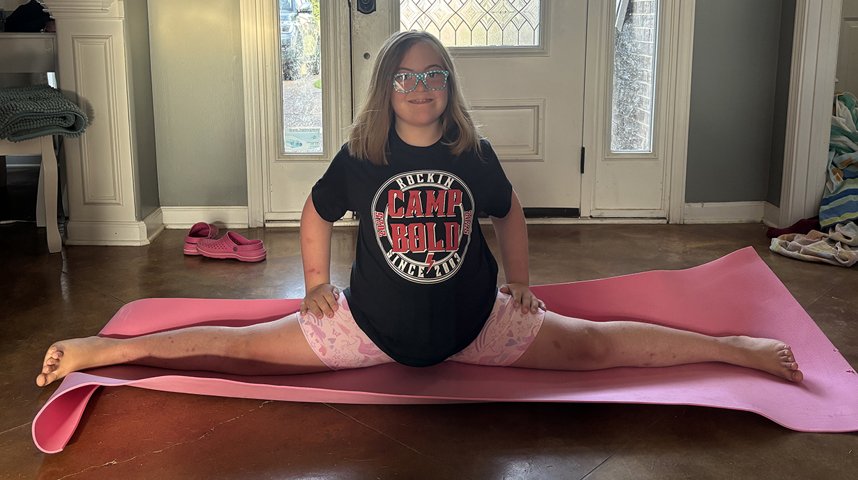 A young girl demonstrates a split on a yoga mat.