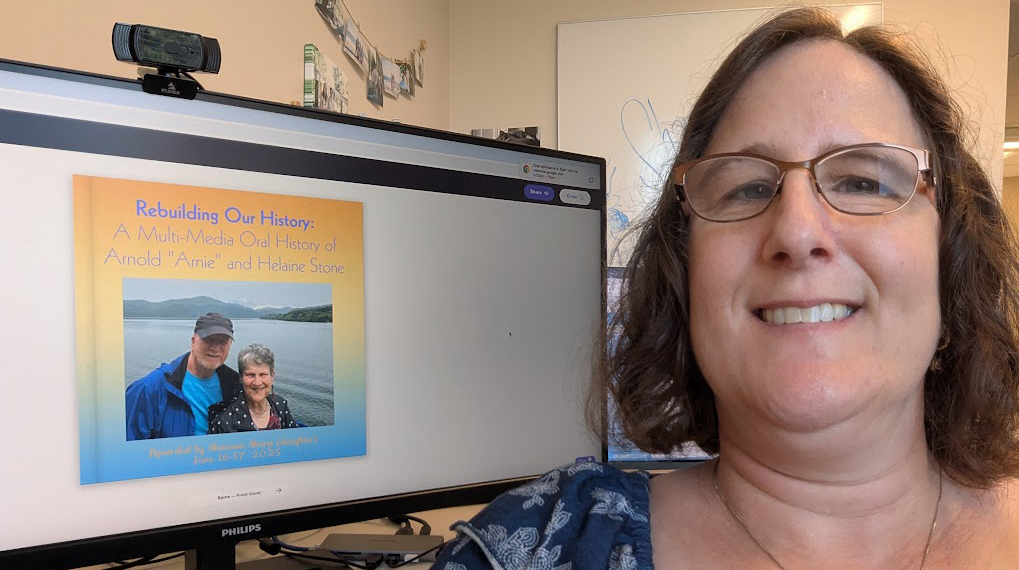 A woman sits beside a computer display of a book cover design.