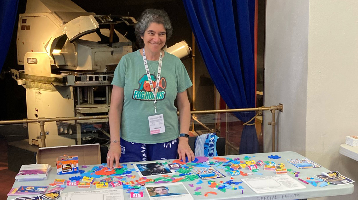 A woman stands behind a table covered with colorful flyers.