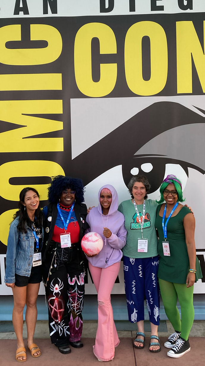 Five women stand in front of a giant Comic-Con mural.