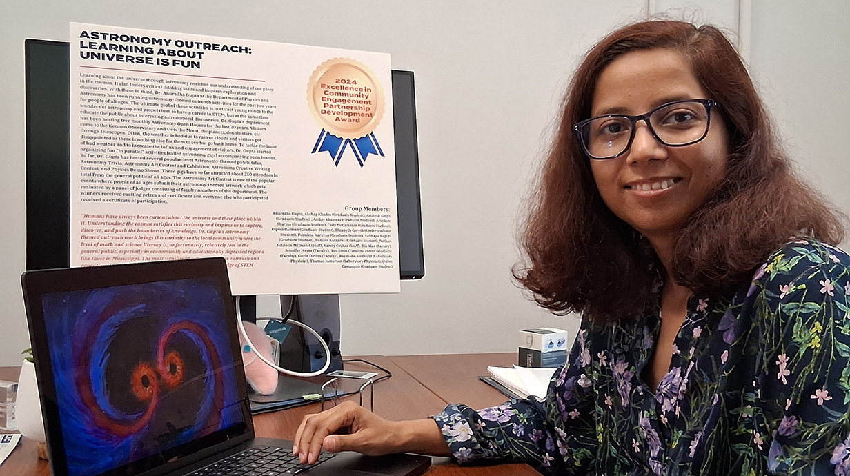 A woman sits at a computer displaying text and graphics about astrophysics research and education.