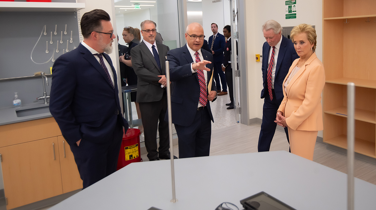 A man points out features of a laboratory to a woman while other people watch.