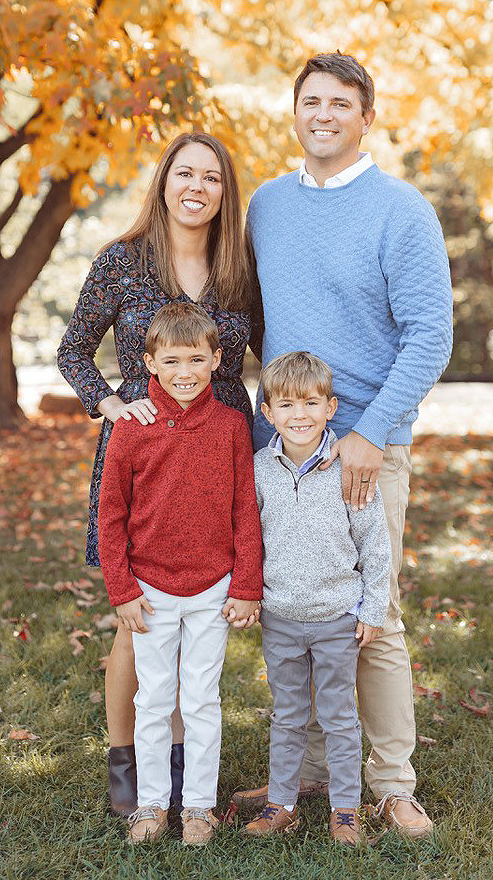 A woman, a man and two young boys pose for an outdoor photo in front of colorful fall foliage.