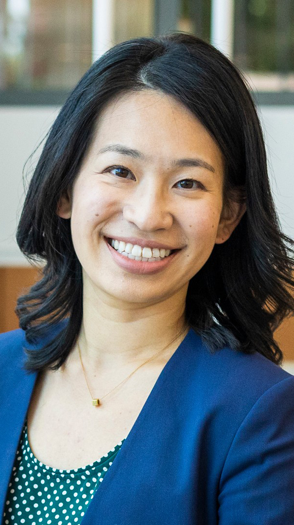 Headshot of a woman wearing a blue jacket over a green polka-dotted dress.