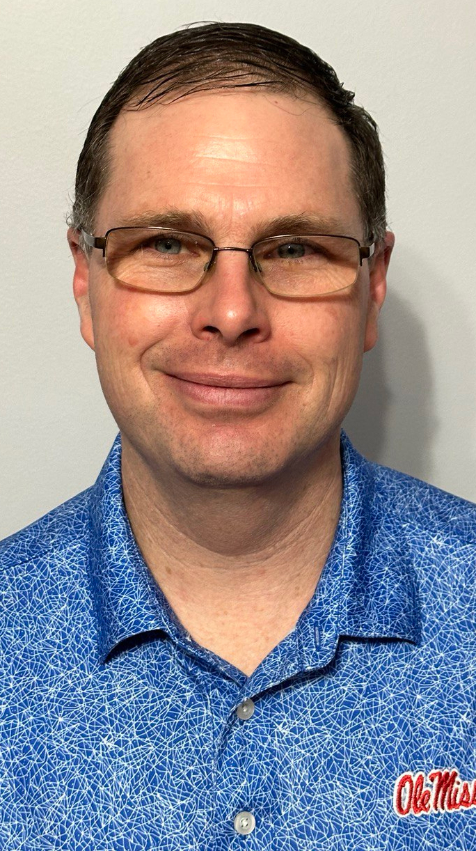 Headshot of a man wearing glasses and a blue polo shirt.