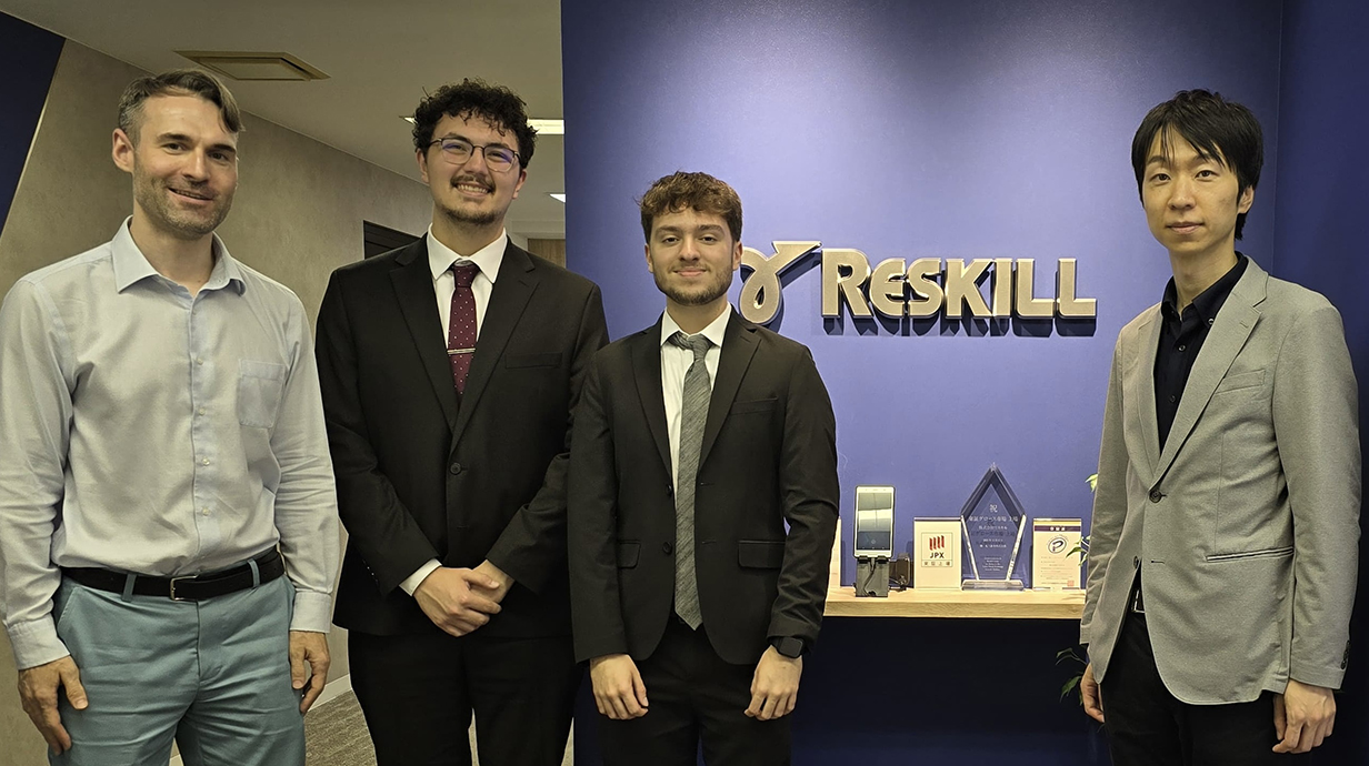 Four young men wearing business attire stand in a hallway at an office.