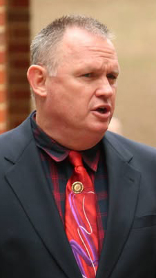 Photo of a man wearing a black jacket and a red necktie.