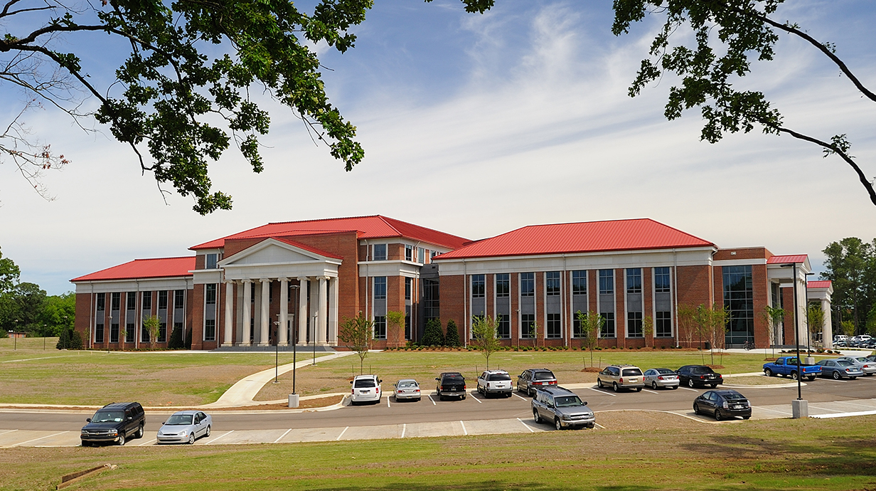 Photo of a large brick building with white columns and a parking lot in front.